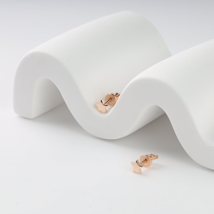 Rose gold star-shaped earrings on a wavy white surface.