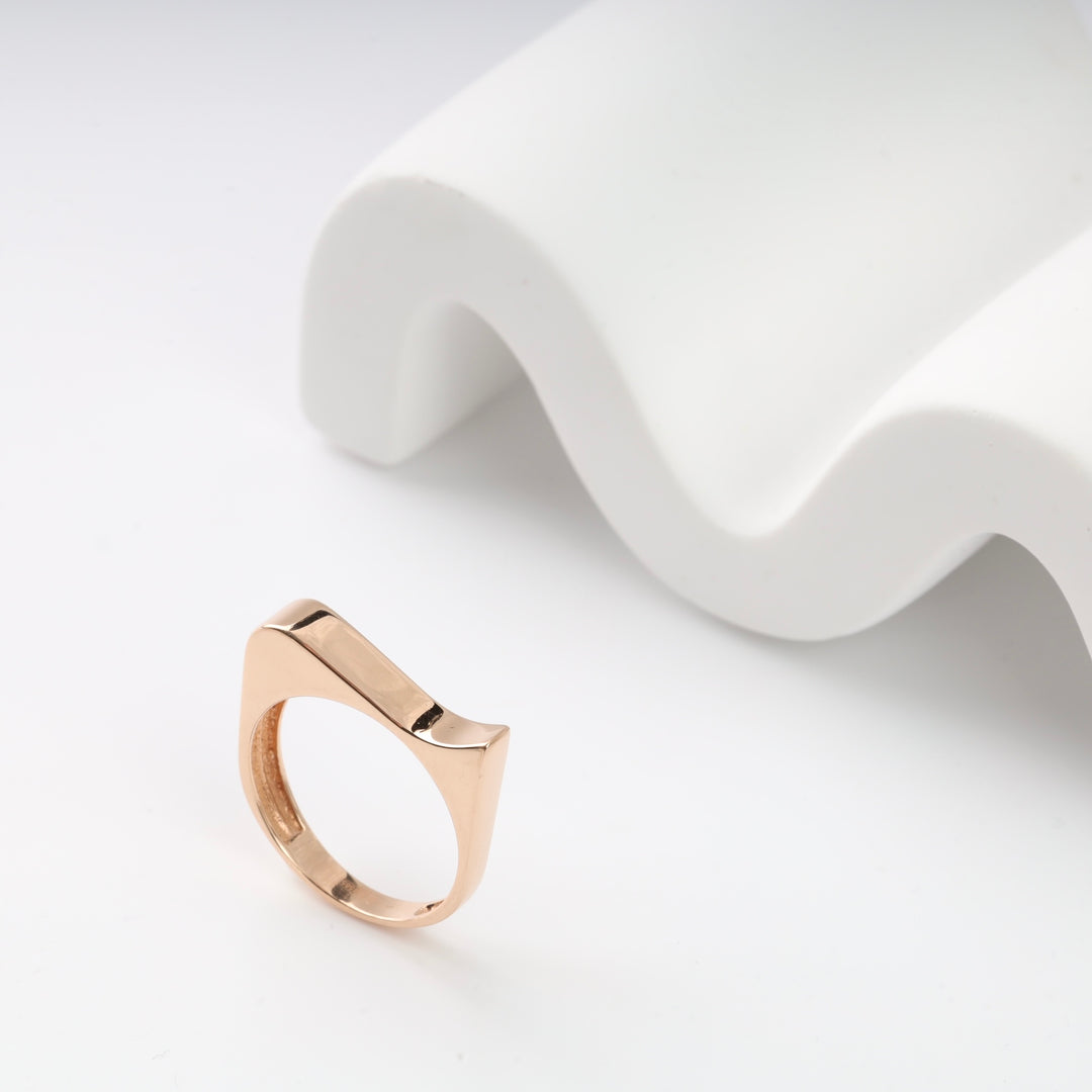 Rose gold geometric ring with a unique wave design displayed on a white sculptural background.