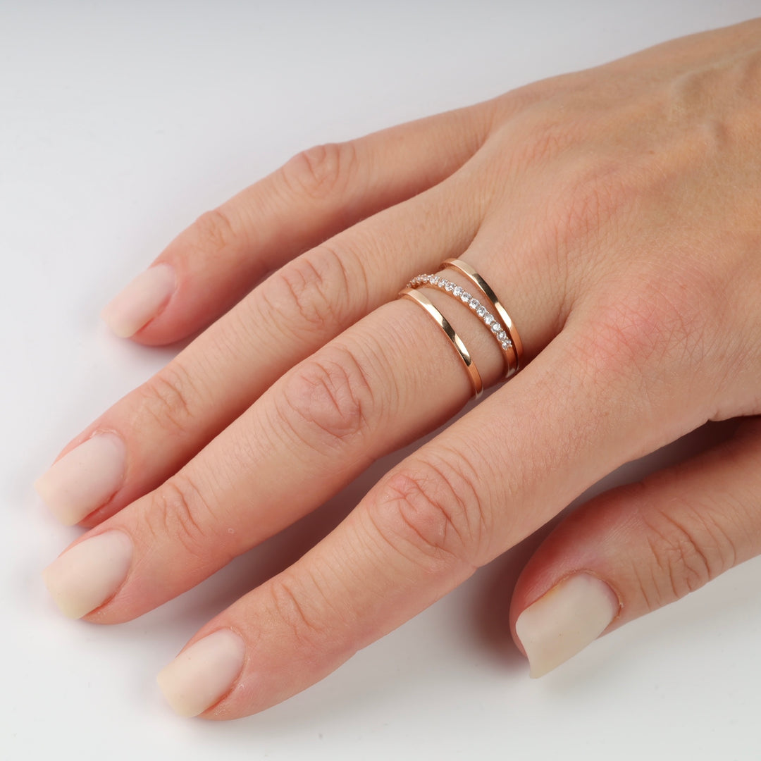 Three rose gold rings with clear stones on a hand.