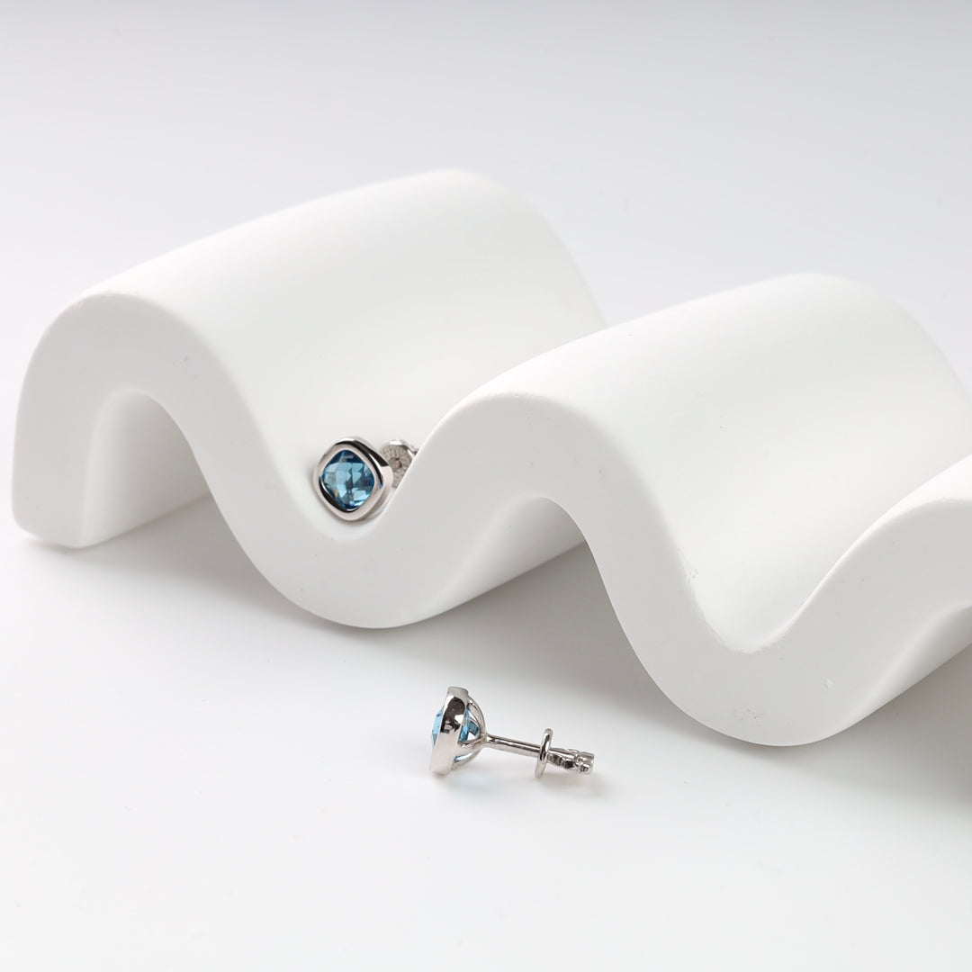 Silver stud earrings with blue gemstones on a white wavy display.