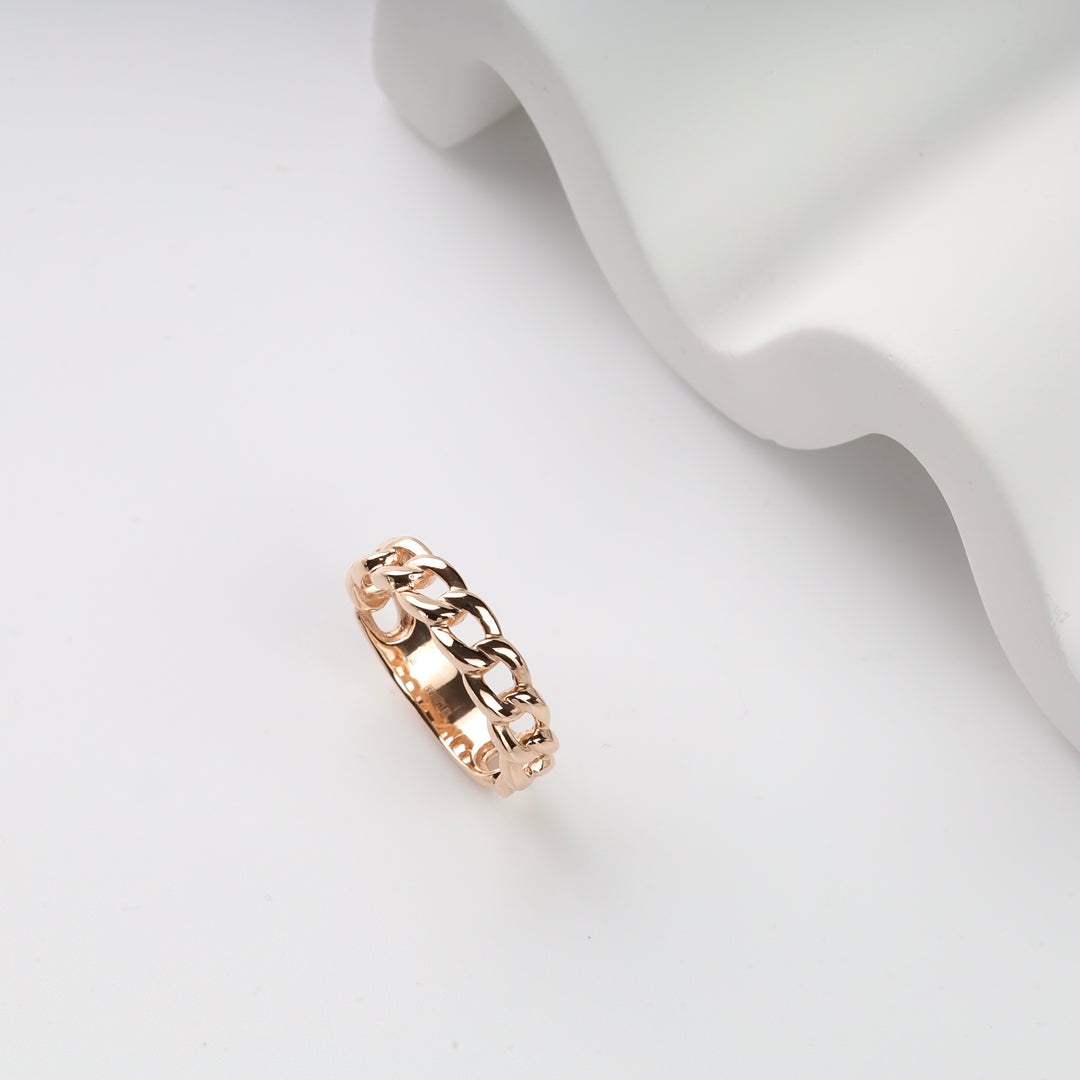 Gold chain link ring on white textured background.