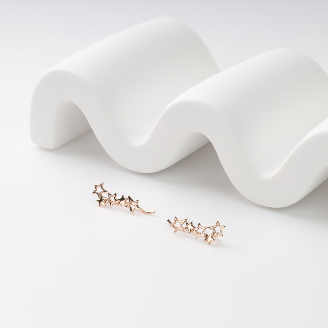 Pair of rose gold star ear climbers with five hollow stars each on a white wavy display, rose gold earrings.