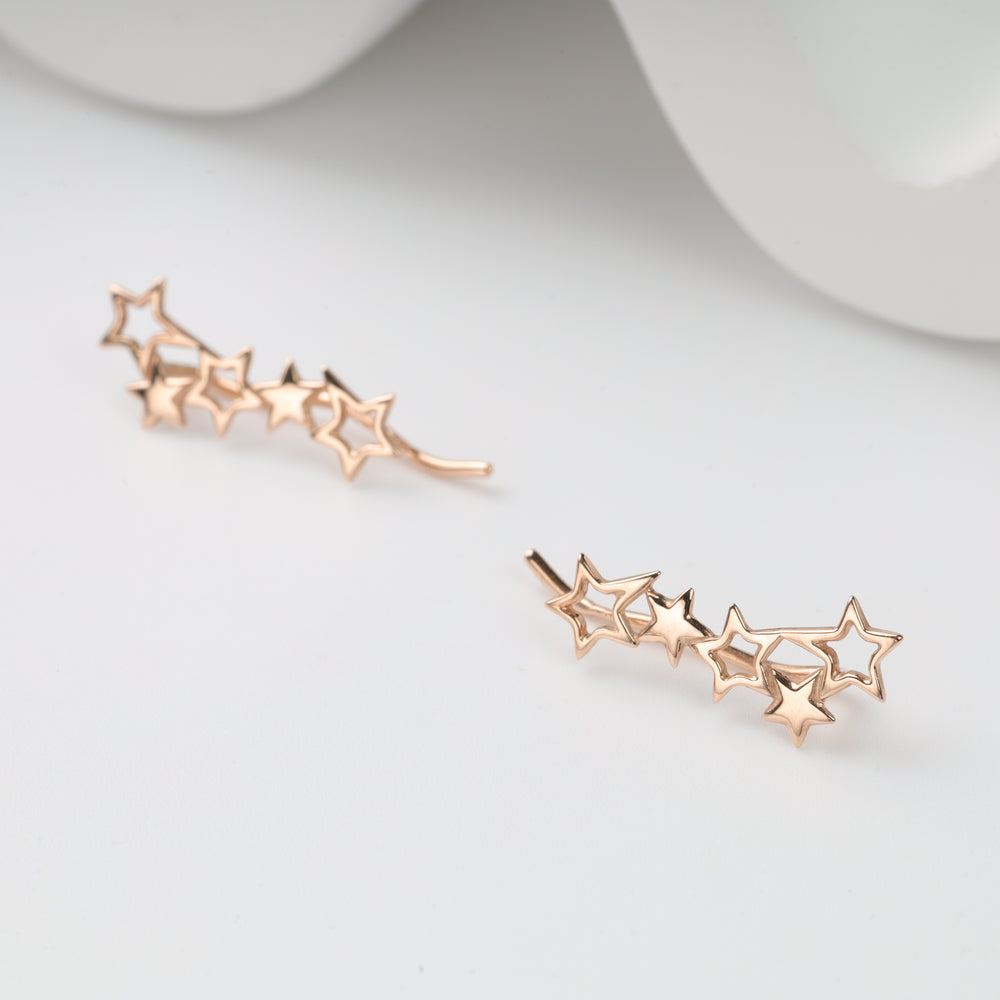Pair of rose gold star ear climbers with five linked stars, metal star earrings displayed on a white surface.