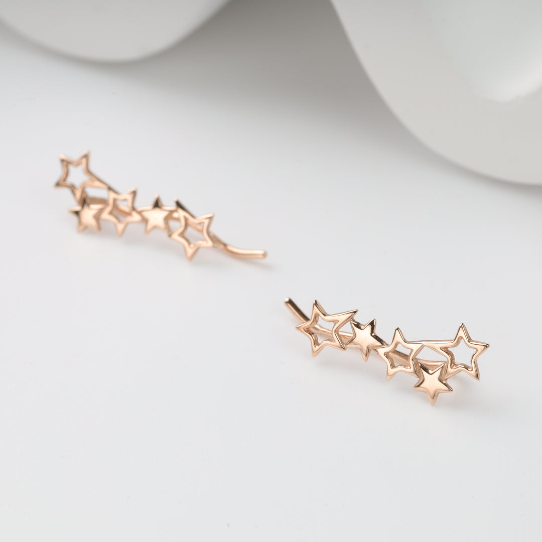 Pair of rose gold star ear climbers with five linked stars, metal star earrings displayed on a white surface.