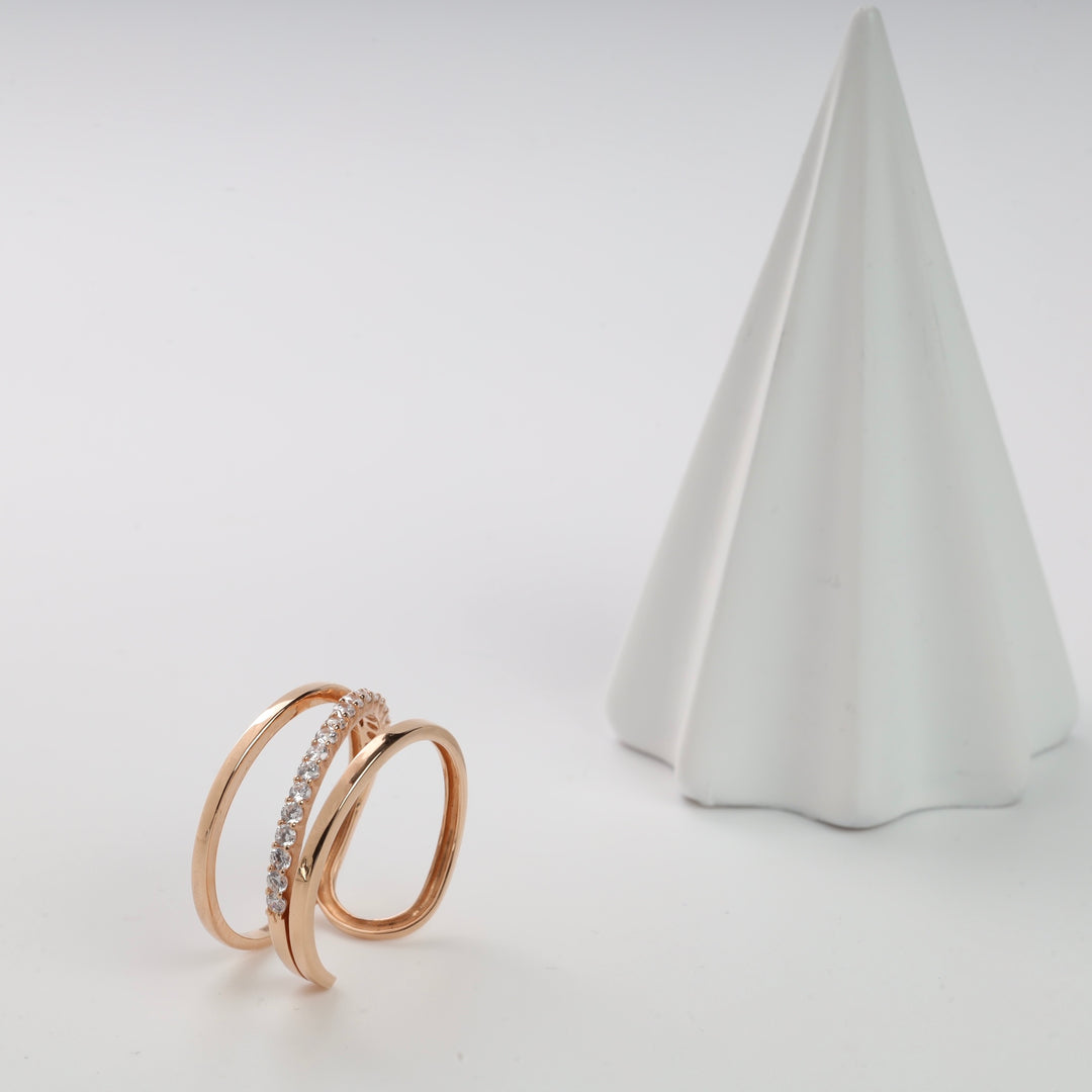 Rose gold triple band ring with cubic zirconia stones on display near a white cone.
