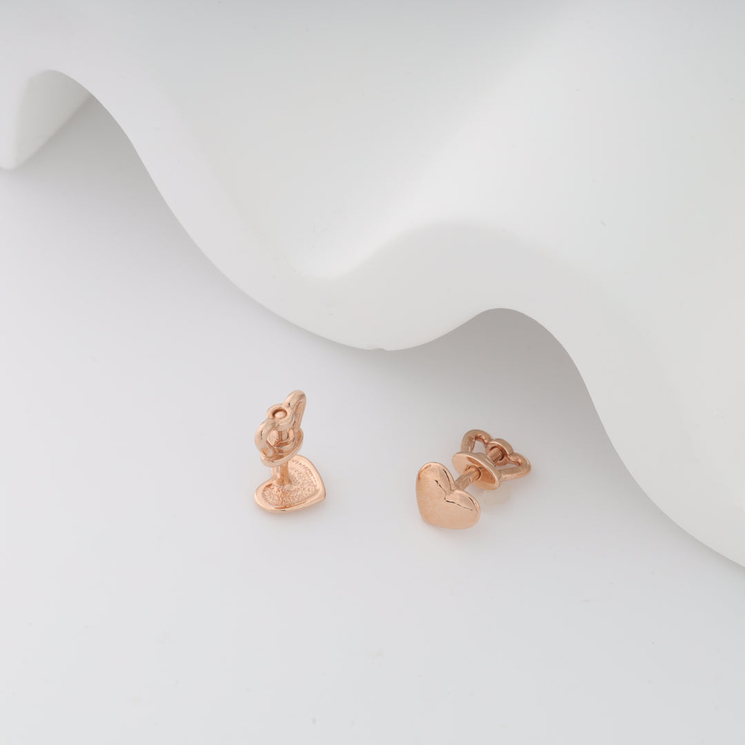 Rose gold heart stud earrings on a white textured surface.