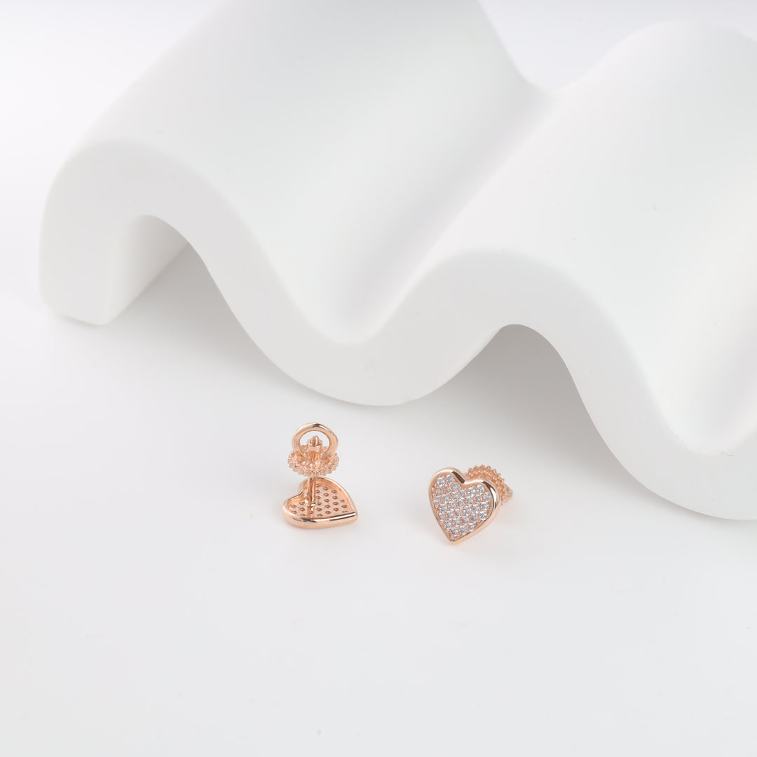 Rose gold heart-shaped stud earrings with clear crystals displayed on a white wave backdrop.
