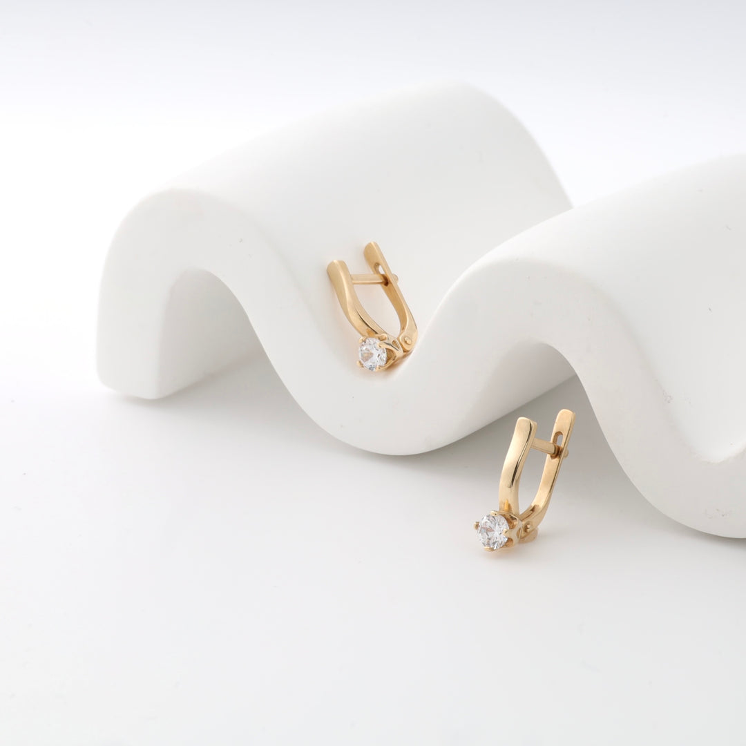 Gold hoop earrings with crystal stones displayed on a white wavy surface.