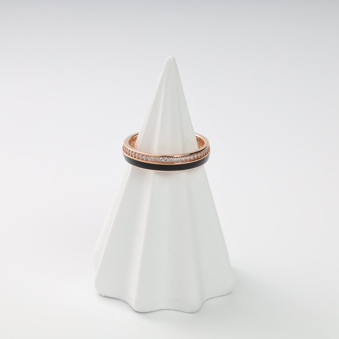 A rose gold and black enamel ring with crystal accents displayed on a white cone stand.