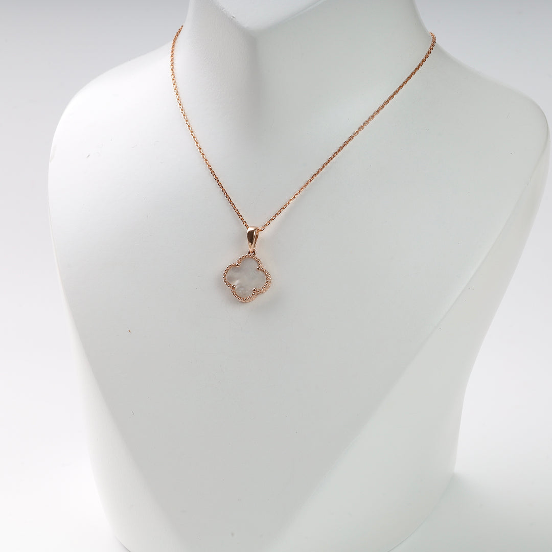 Gold chain necklace with a clover-shaped pendant and white center displayed on a white bust. Gold clover necklace.