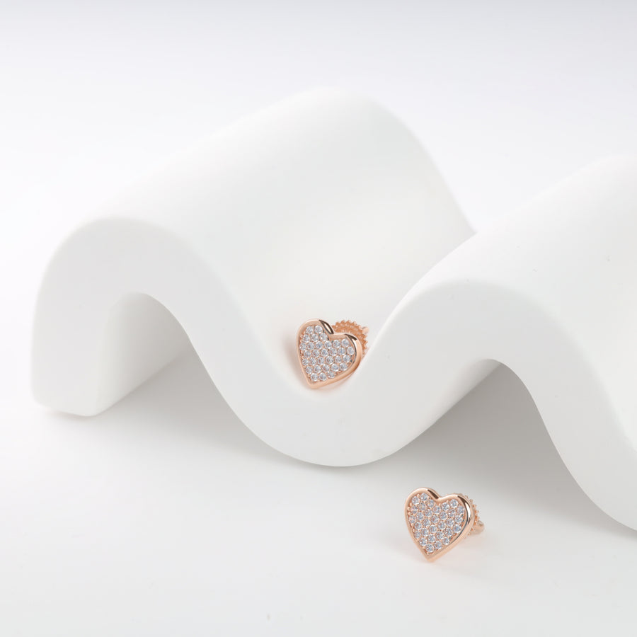 Rose gold heart-shaped stud earrings with crystal embellishments on a white wave-pattern display.