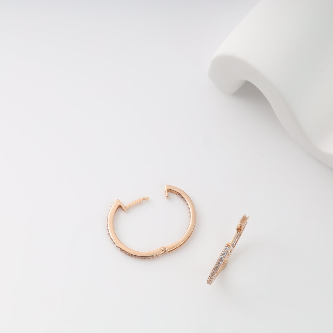 Rose gold hoop earrings with small clear stones, displayed on a white surface.