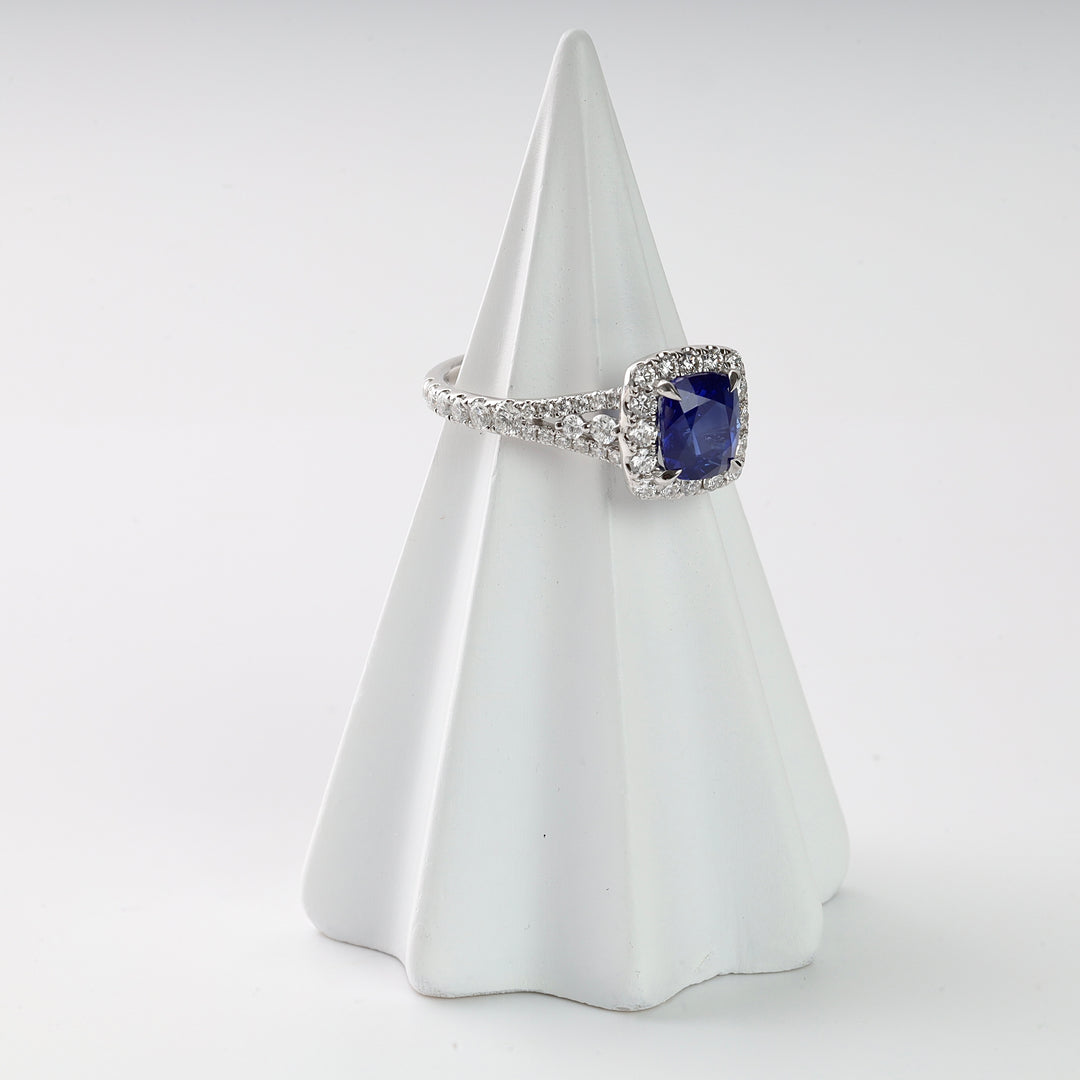 Silver ring with a square blue gemstone and small clear stones displayed on a white ring holder.