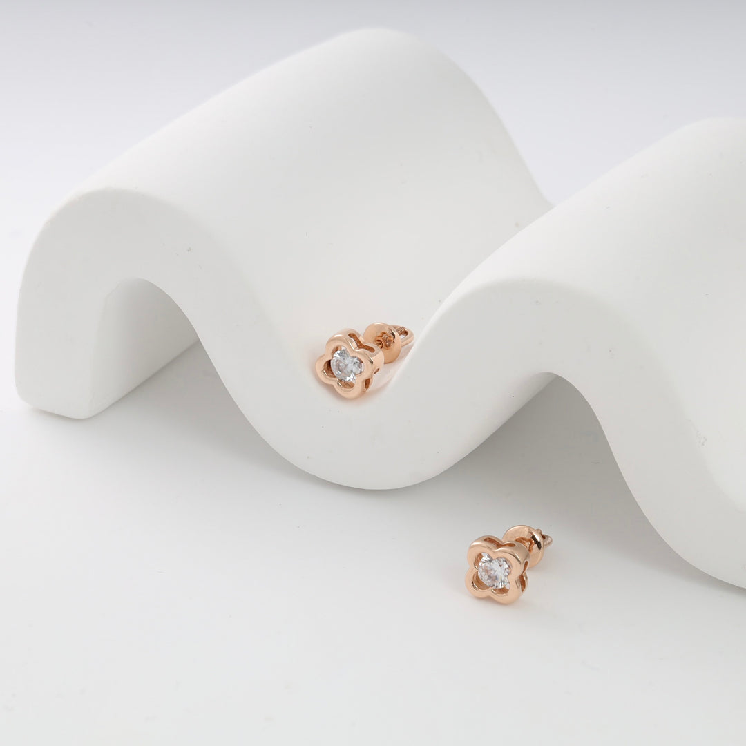 Rose gold stud earrings with clover design and clear stones displayed on a white wavy stand.