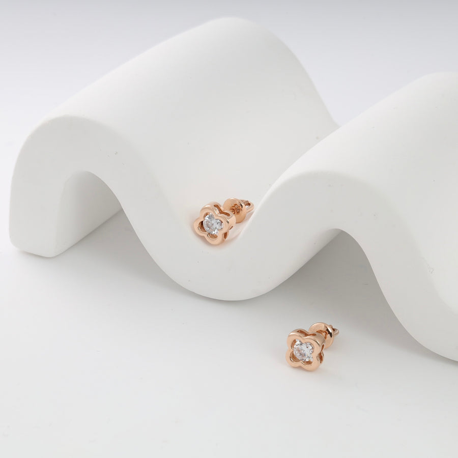 Rose gold stud earrings with clover design and clear stones displayed on a white wavy stand.