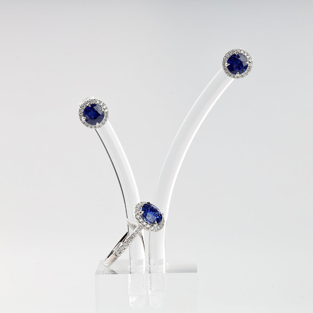 Silver ring and earrings set with blue sapphire stones and small clear accents on a clear display stand.