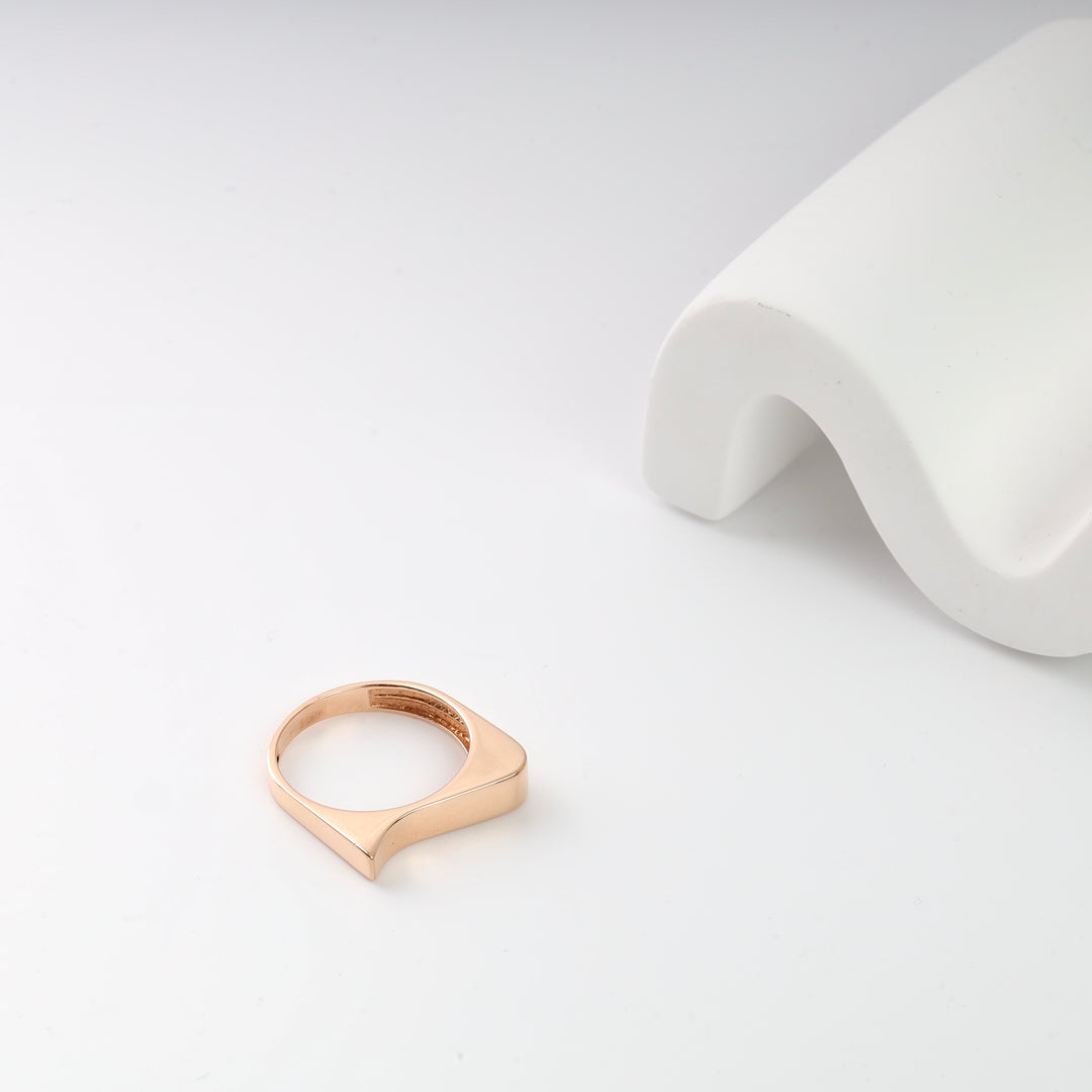 Gold minimalist ring with square design on white curved display.