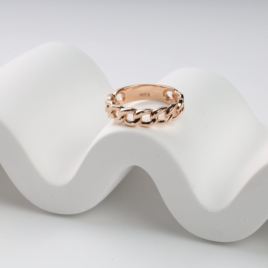 Rose gold chain link ring on white curved surface.