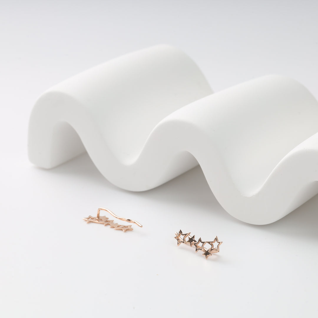 Pair of rose gold star ear climbers with five linked star motifs on a white wavy display, rose gold ear climbers, star earrings.