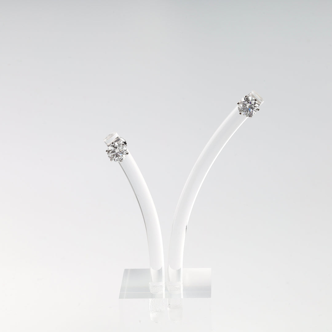 Pair of round white diamond stud earrings in silver settings on a clear acrylic display.