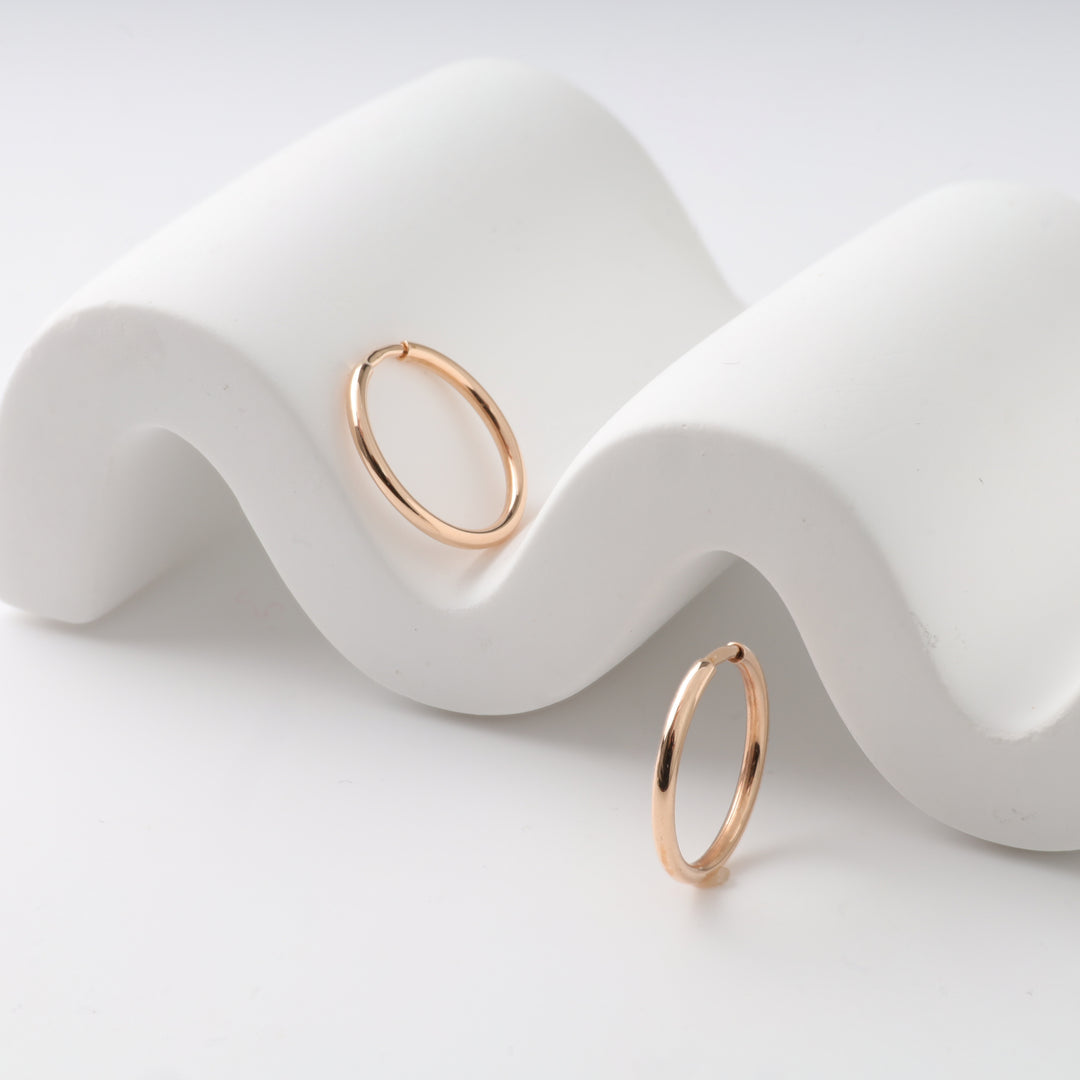 Gold hoop earrings displayed on curved white surface.