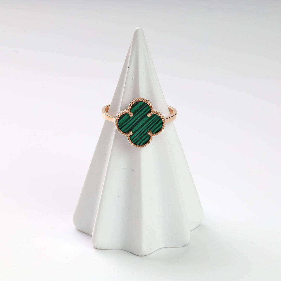 Gold ring with green malachite clover motif displayed on a white ceramic cone, gemstone ring, malachite jewelry.