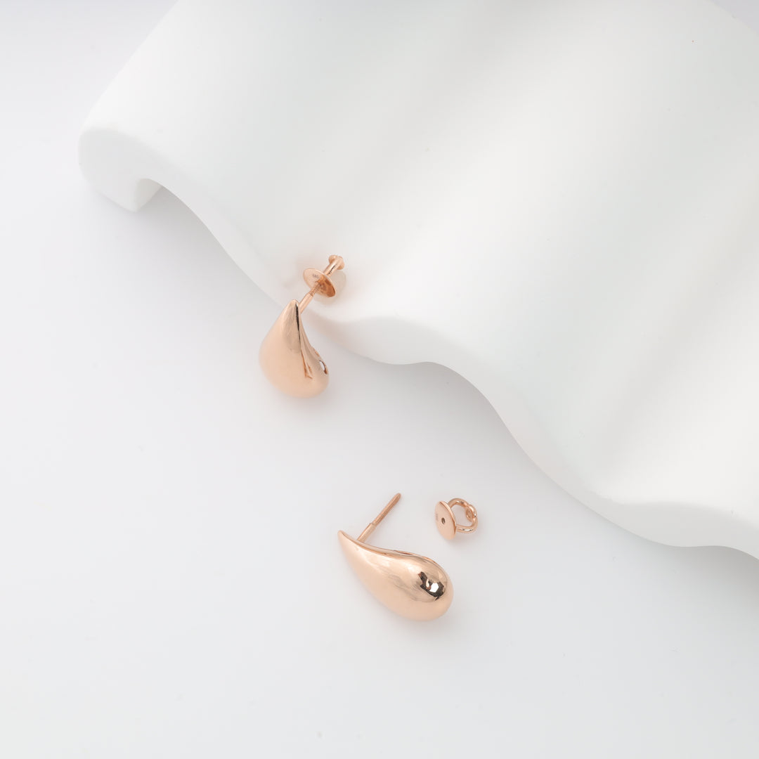 Rose gold teardrop stud earrings displayed as a pair on a white prop with posts and butterfly backs; rose gold stud earrings.