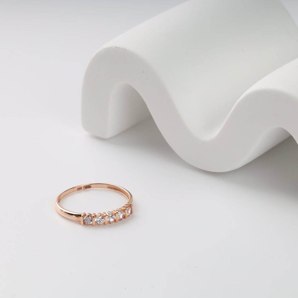 Rose gold ring with five small diamonds on white wave backdrop.