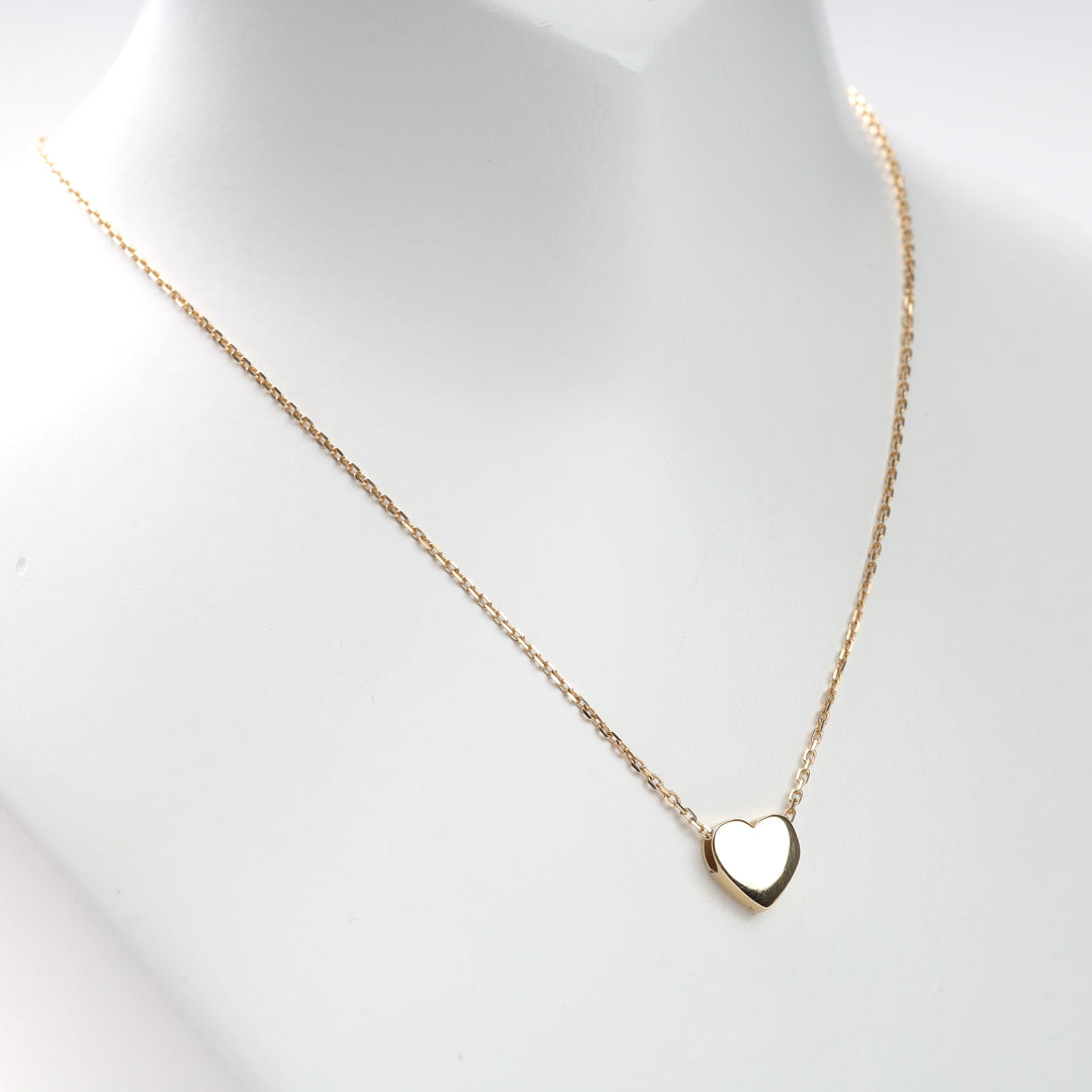 Yellow gold heart pendant necklace on a white display bust, thin yellow gold chain with smooth heart charm, gold heart necklace.