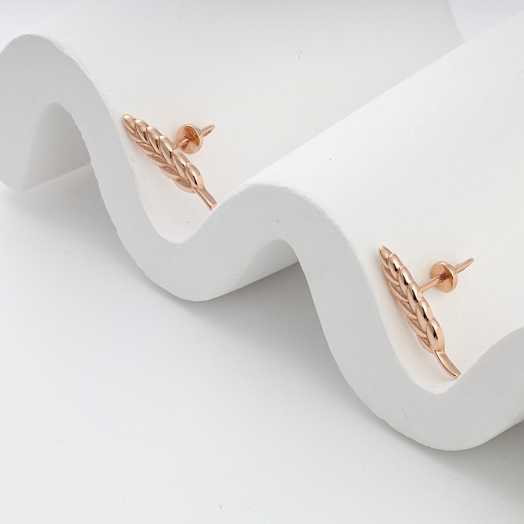 Rose gold wheat motif stud earrings shown on a white wavy surface, jewelry studs, leaf earrings.