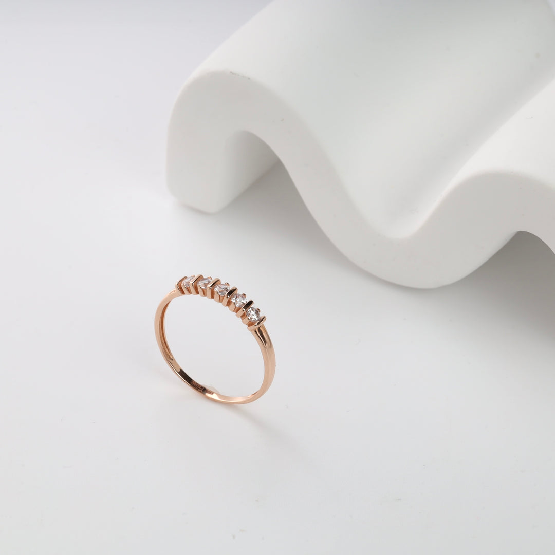 Rose gold ring with five small, round diamonds on a white surface. Elegant jewelry piece, minimalist design.