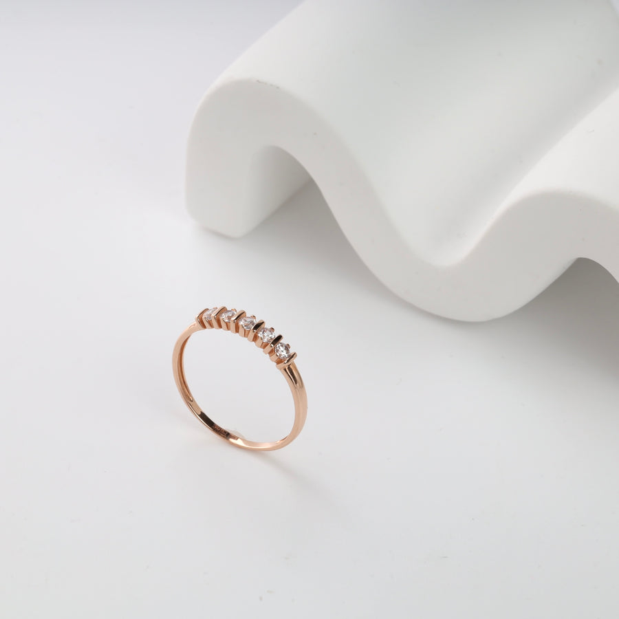 Rose gold ring with five small, round diamonds on a white surface. Elegant jewelry piece, minimalist design.