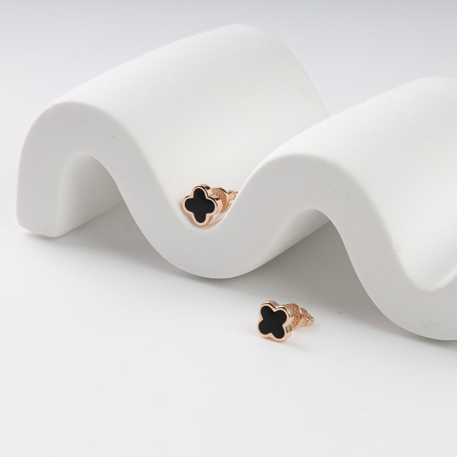 Rose gold and black clover earrings on wavy white surface.