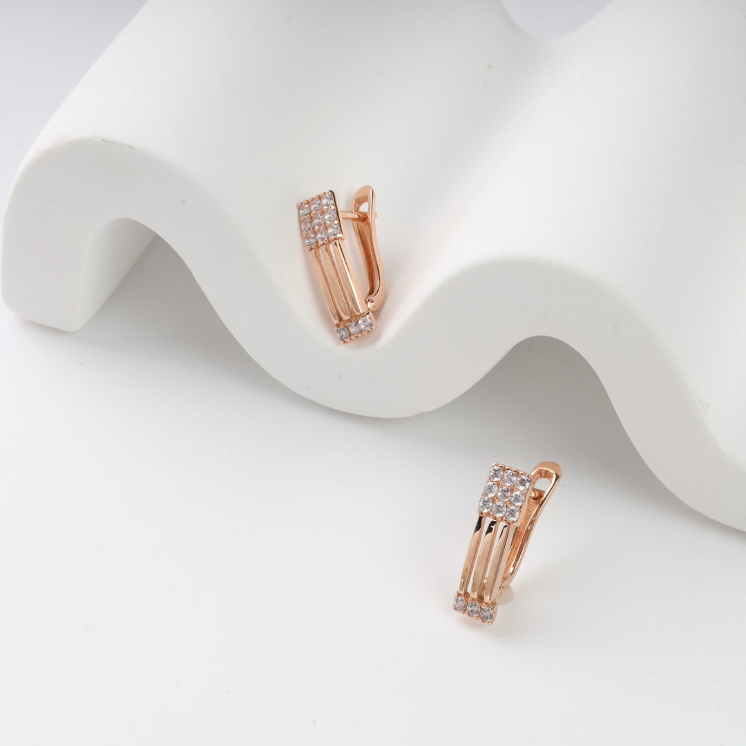 Rose gold earrings with crystal accents displayed on a white wavy surface.