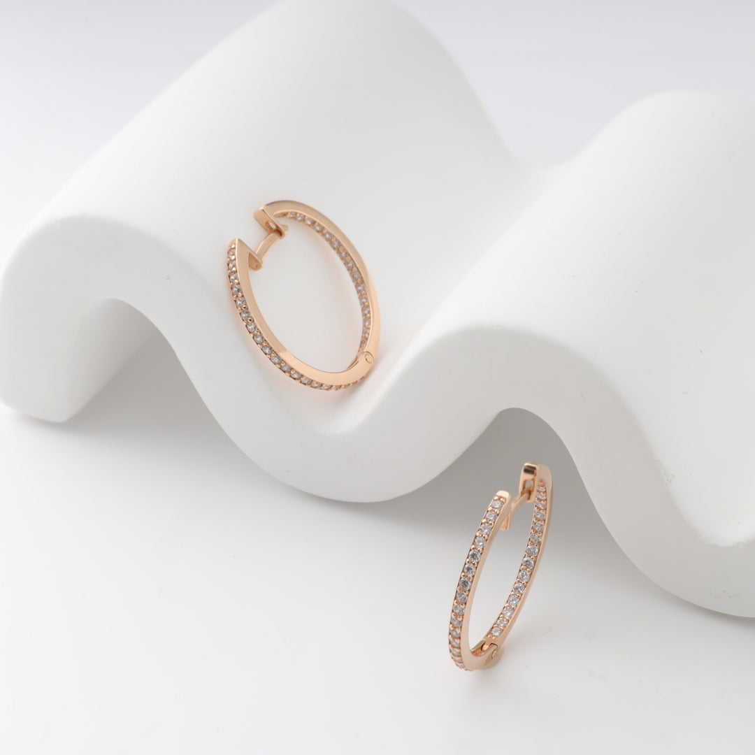 Rose gold hoop earrings with sparkling stones on a wavy white backdrop.