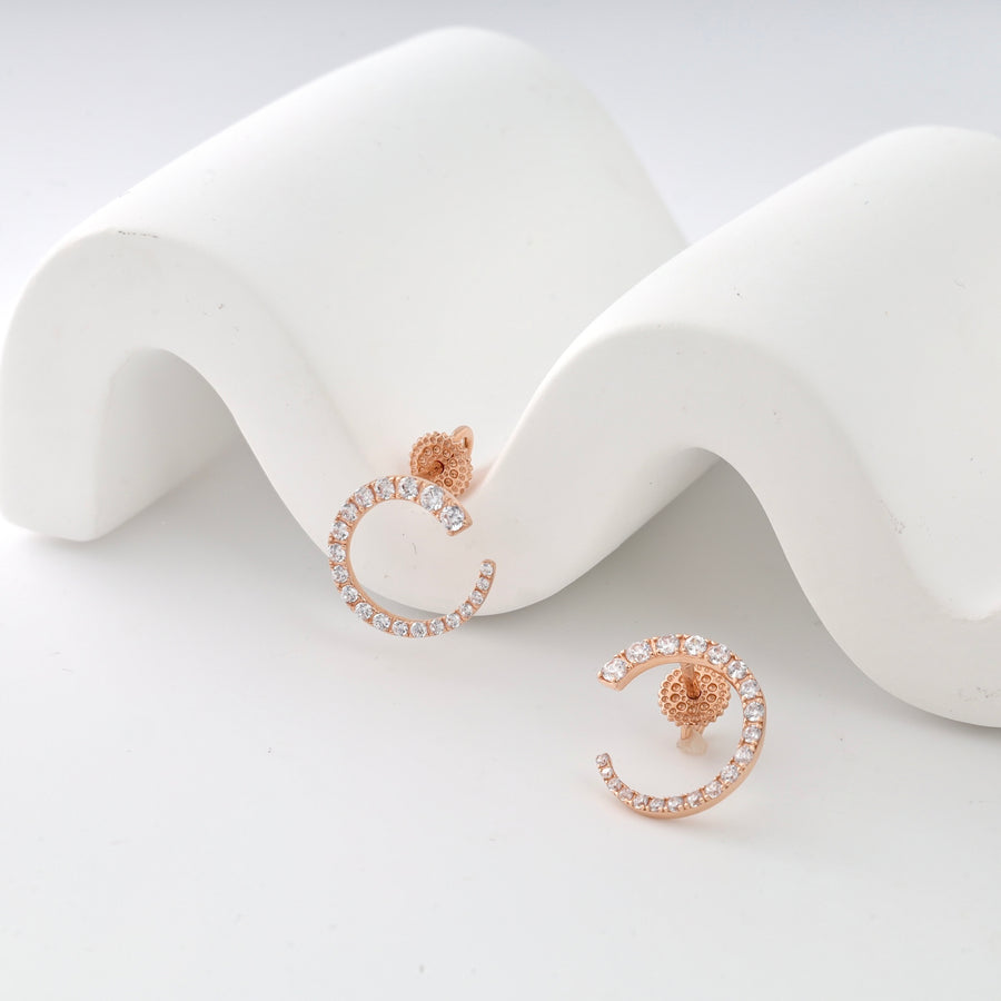 Rose gold earrings with crystal accents in a crescent shape on white curved display.