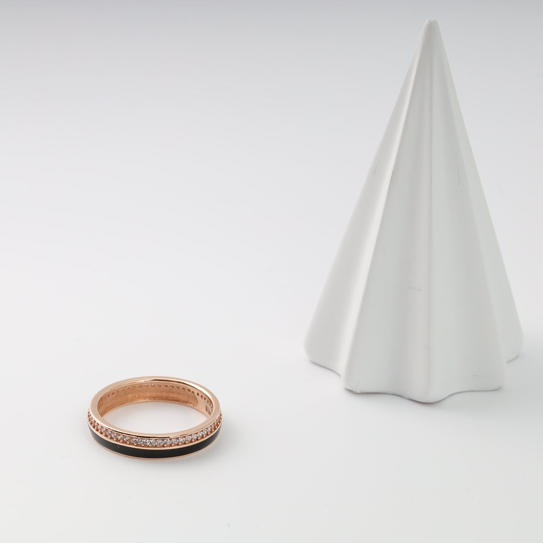 Rose gold ring with black inlay and cubic zirconia accents beside a white cone display.