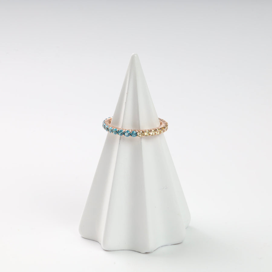 Gold ring with blue and yellow gemstones displayed on a white ceramic cone.