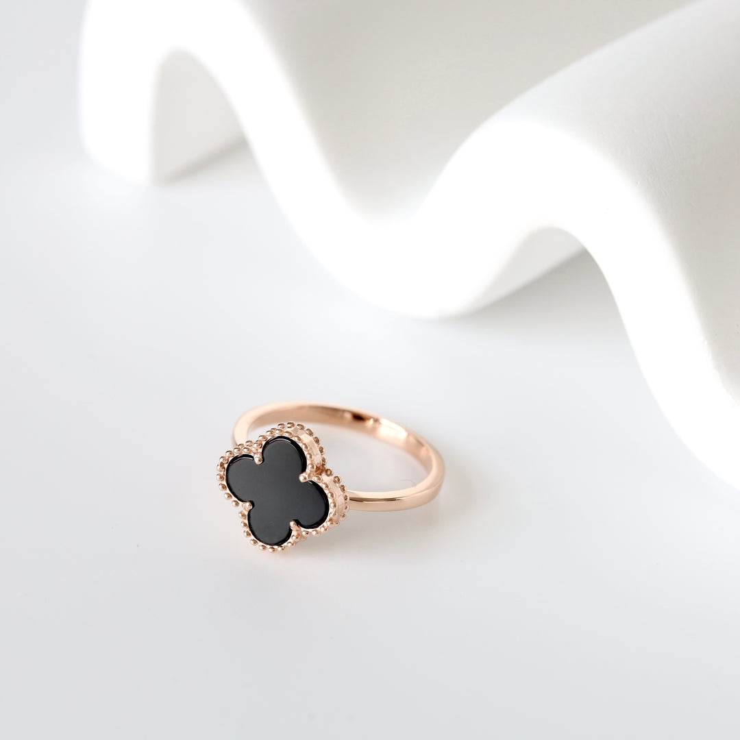 Rose gold ring with a black quatrefoil motif, beaded edges, shown against a white background.