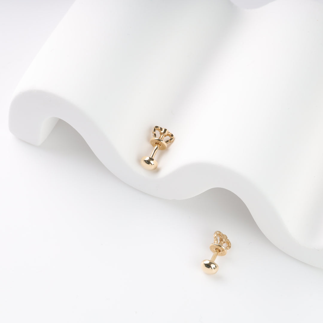 Gold crown-shaped stud earrings on a white wavy surface.