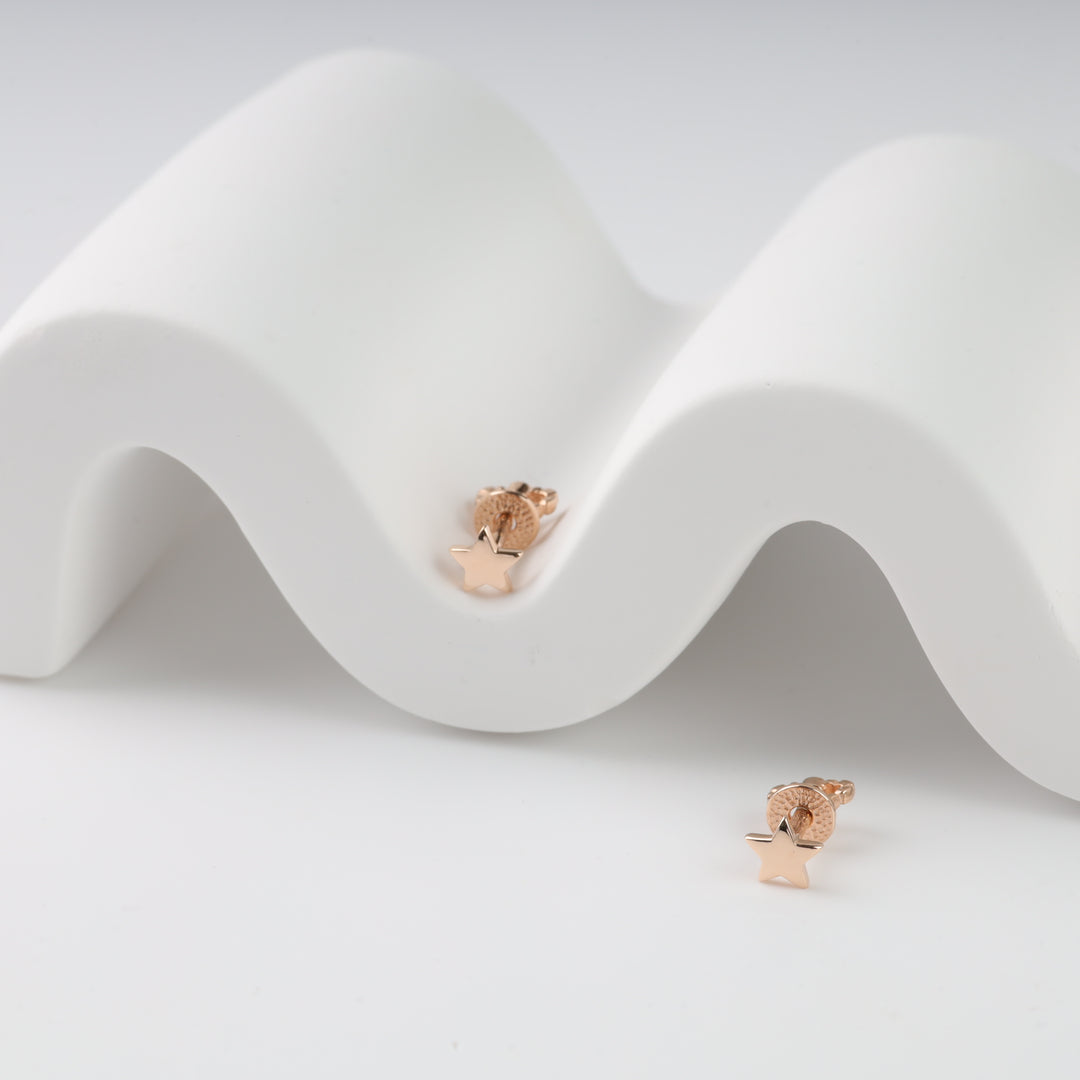 Rose gold star stud earrings on a white wavy surface.