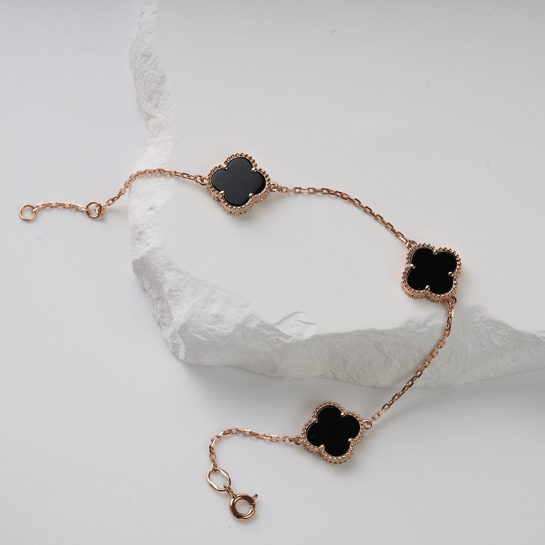 Gold chain bracelet with three black clover-shaped charms displayed on white stone.