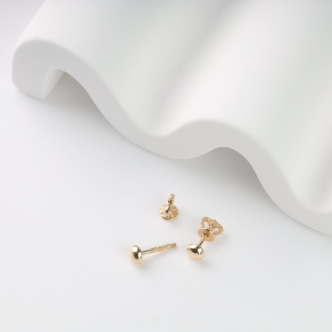 Gold stud earrings on a white wavy backdrop.
