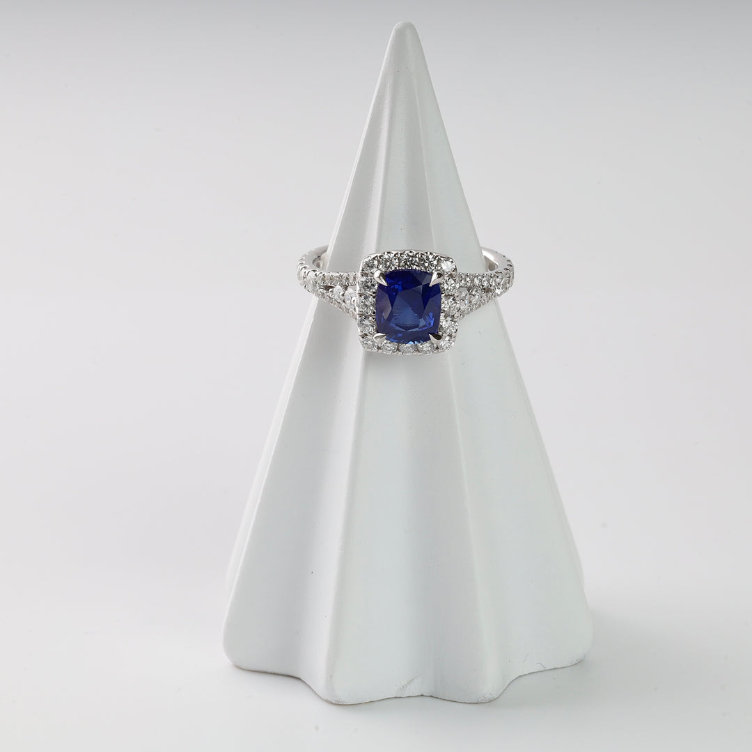 Square blue gemstone and clear crystal silver ring displayed on a white ring cone stand, engagement ring jewelry.