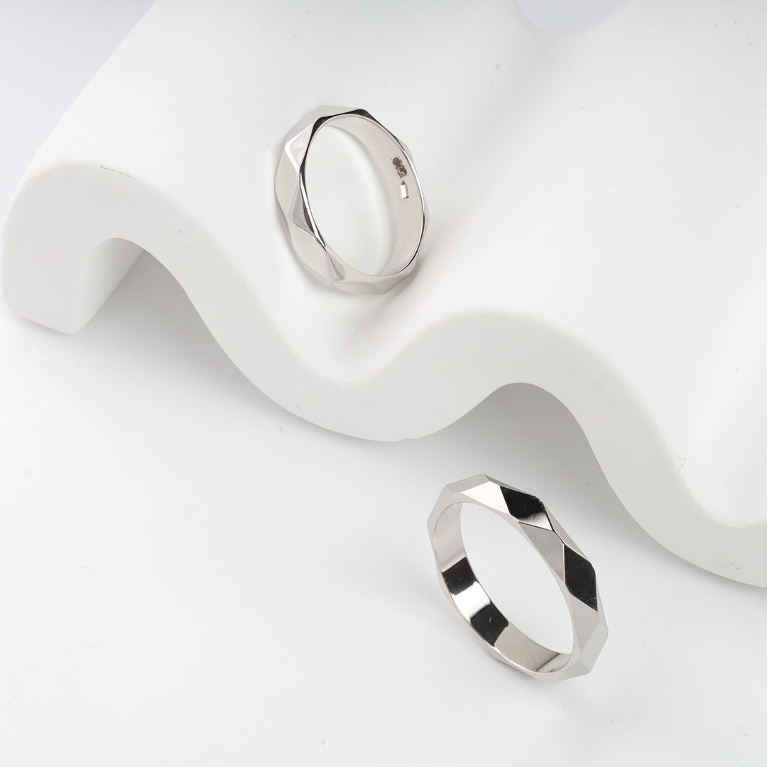 Two silver geometric rings displayed on a white wavy surface.