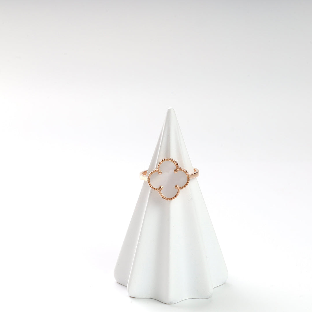 Gold clover motif ring with white enamel sits on a white cone ring holder, jewelry, minimalist ring.