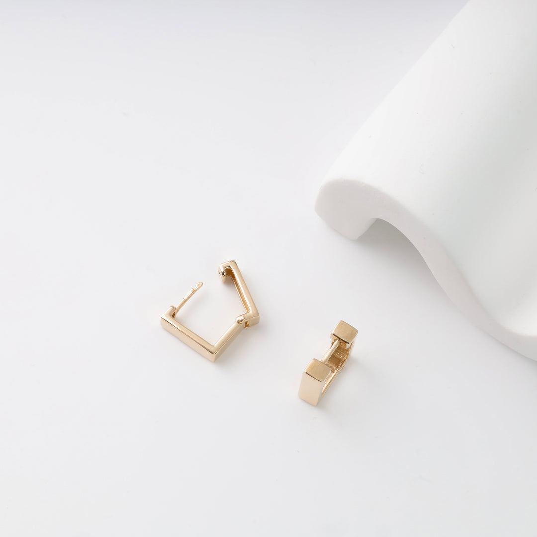 Gold square hoop earrings on a white surface.