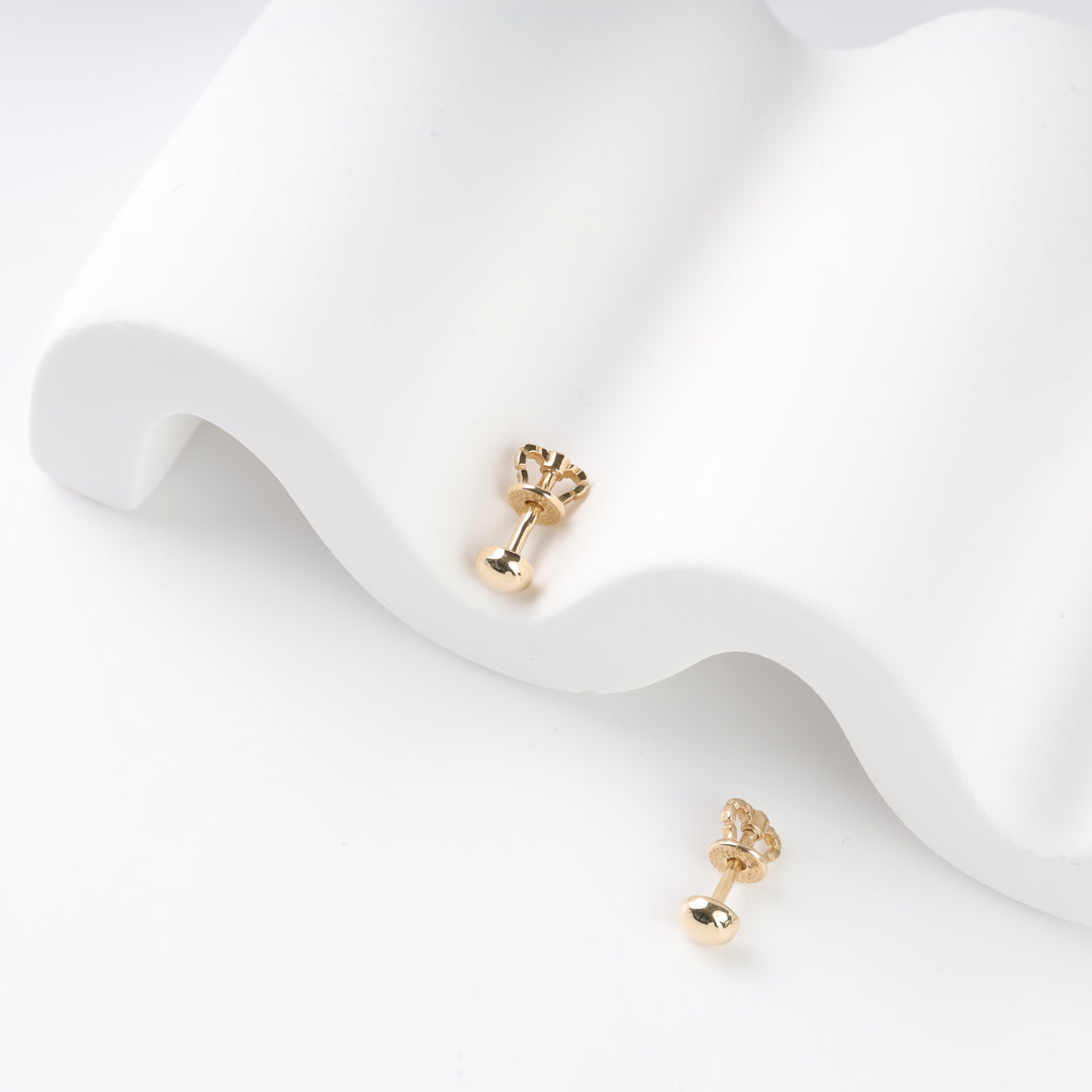 Gold stud earrings with round backs on a curved white surface.