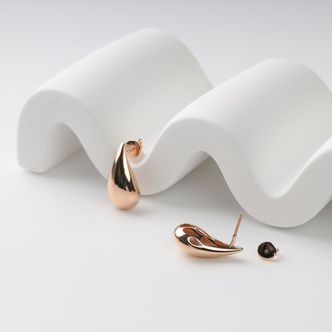 Rose gold teardrop stud earrings on a white wavy display with one loose earring back, rose gold stud earrings, teardrop earrings.