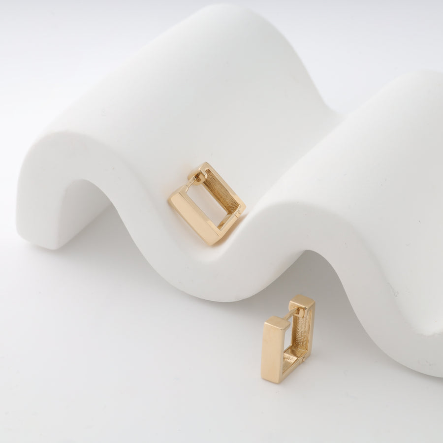 Gold square hoop earrings displayed on a wavy white stand.